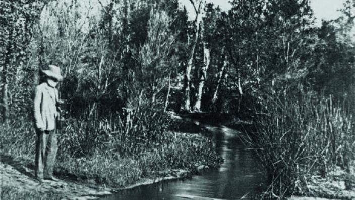 Black and white photo of man standing at lake